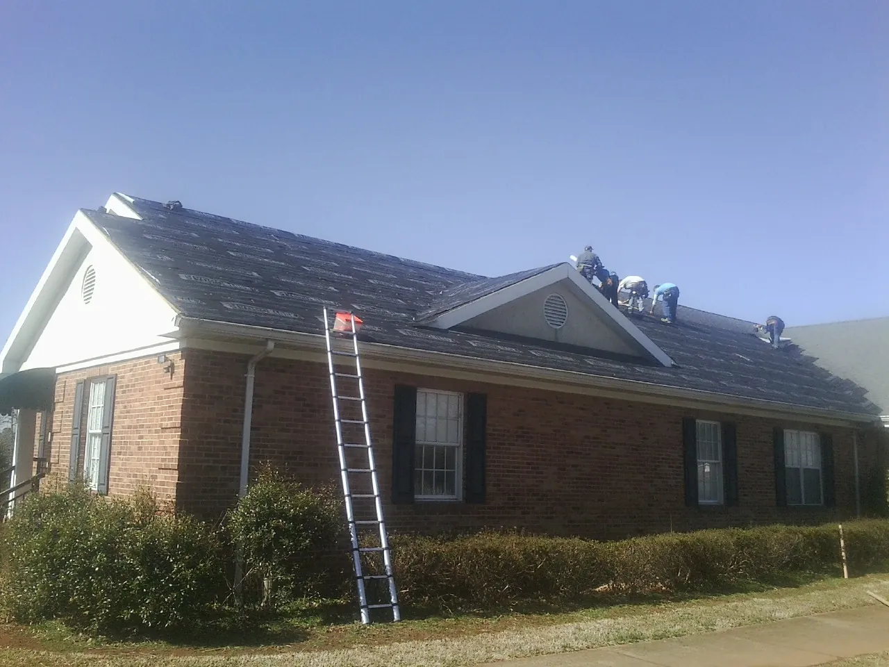 Crew tearing shingles off a brick ranch roof with a ladder set — Emergency Roof Repair work by our crew in Salt Point