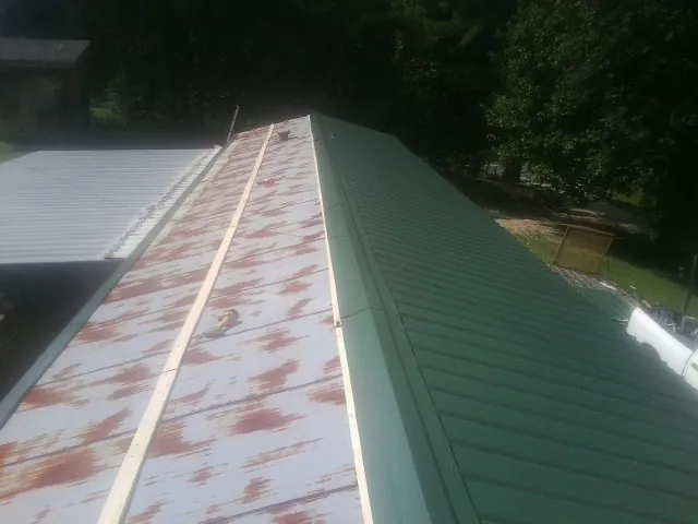 Old rusted panels beside newly installed green metal roofing — Wind Damage Roof Repair by Roofing Brothers in Salt Point