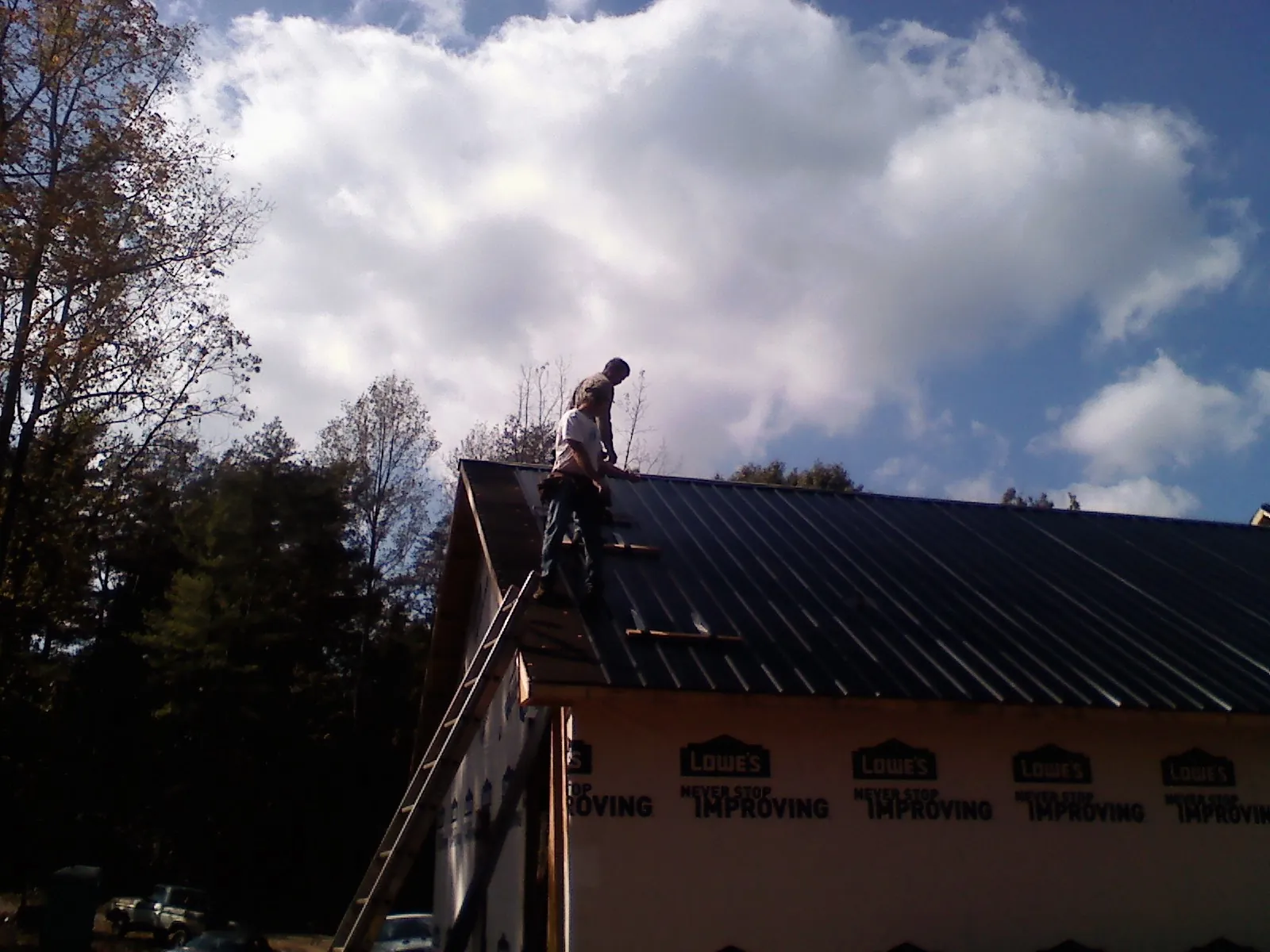 Roofer fastening dark metal panels high against a cloudy sky, from a Roof Inspection job in Salt Point